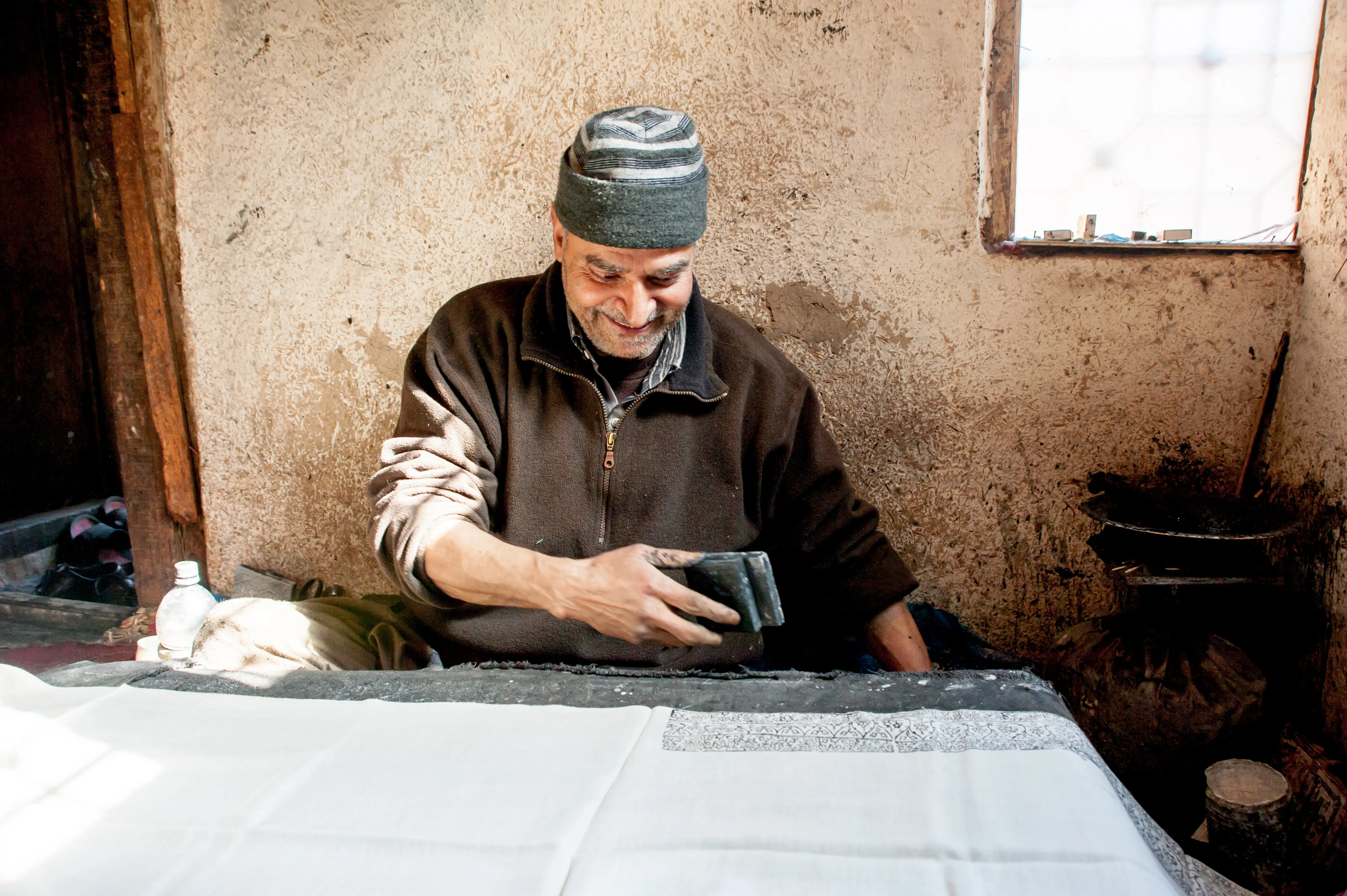 A smiling artisan in a workshop, holding a hand block-printed textile