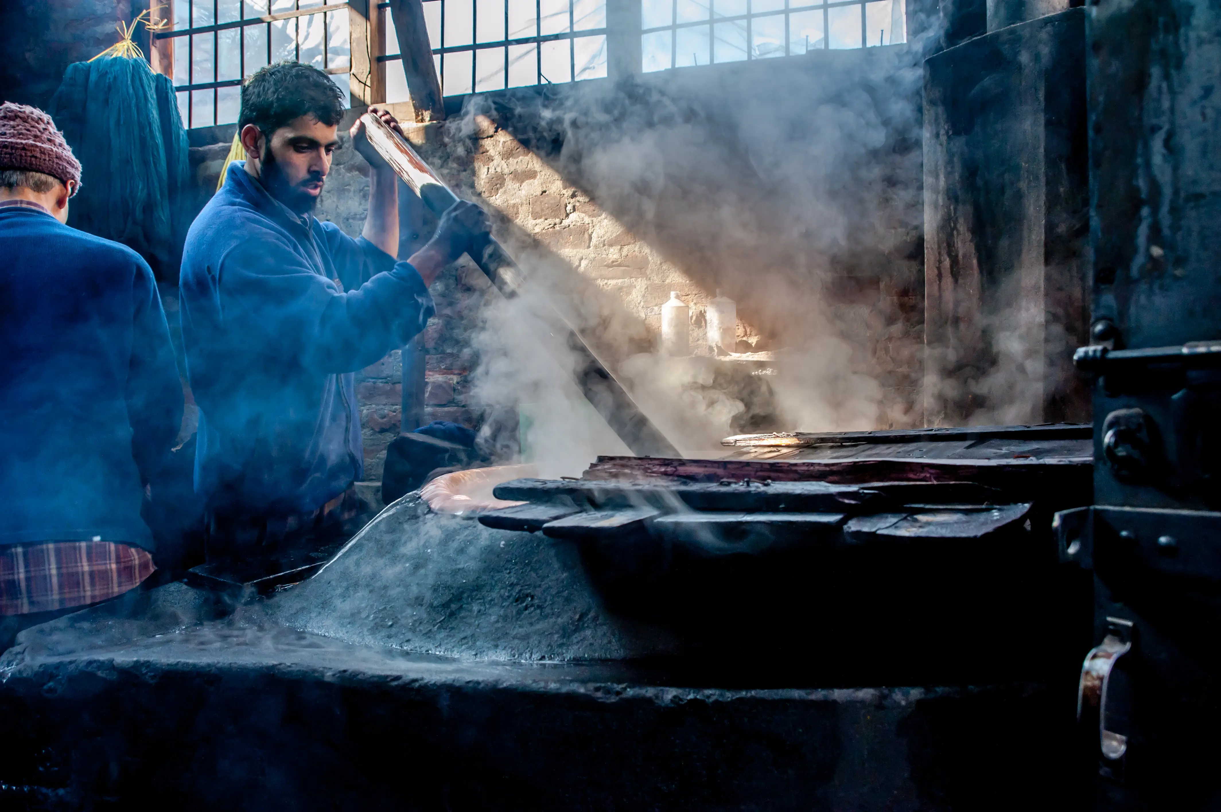 An artisan lifting dyed fabric from a steaming vat in a Srinagar workshop