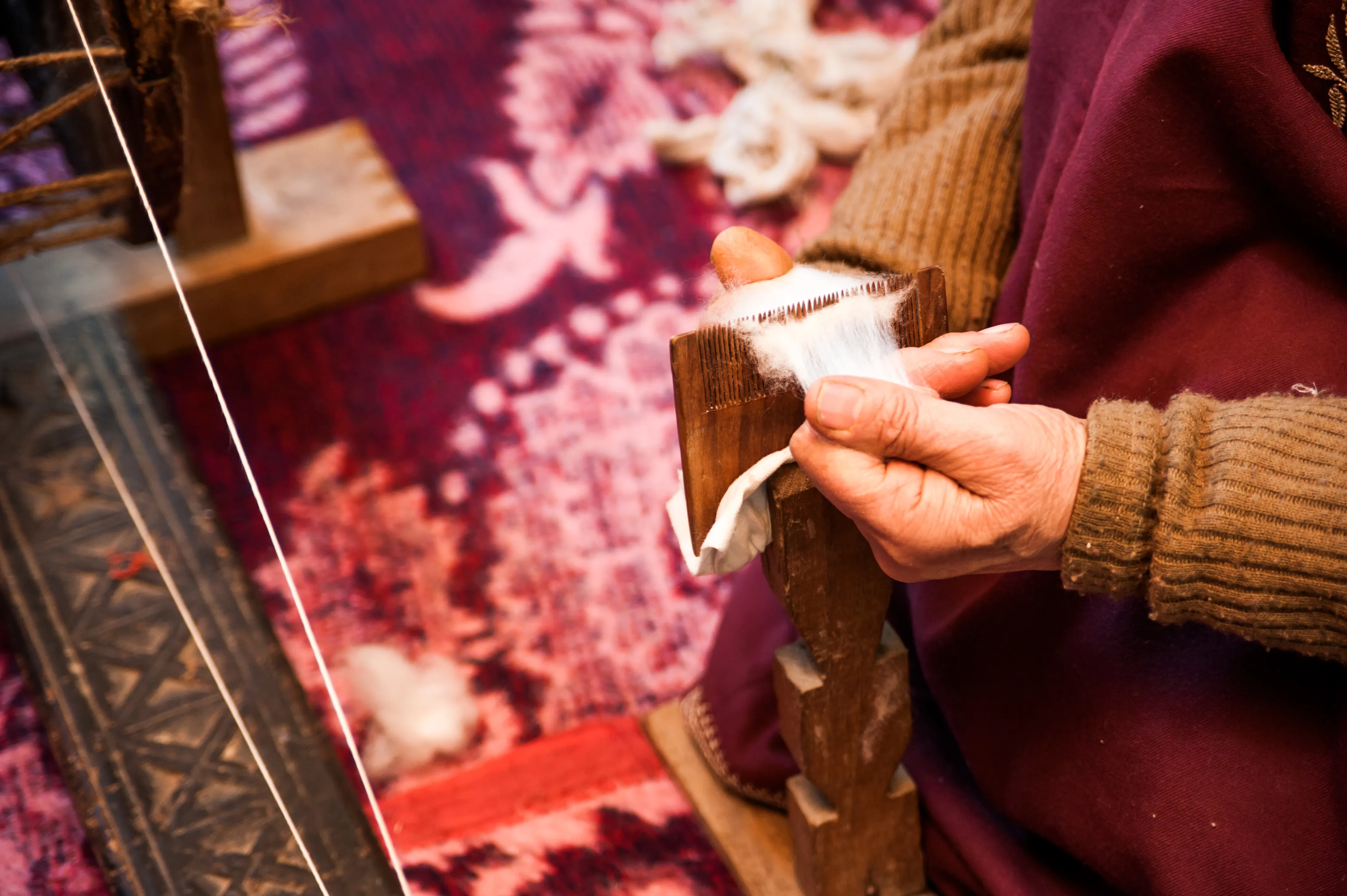 Hands carding raw pashmina fibre with a wooden card