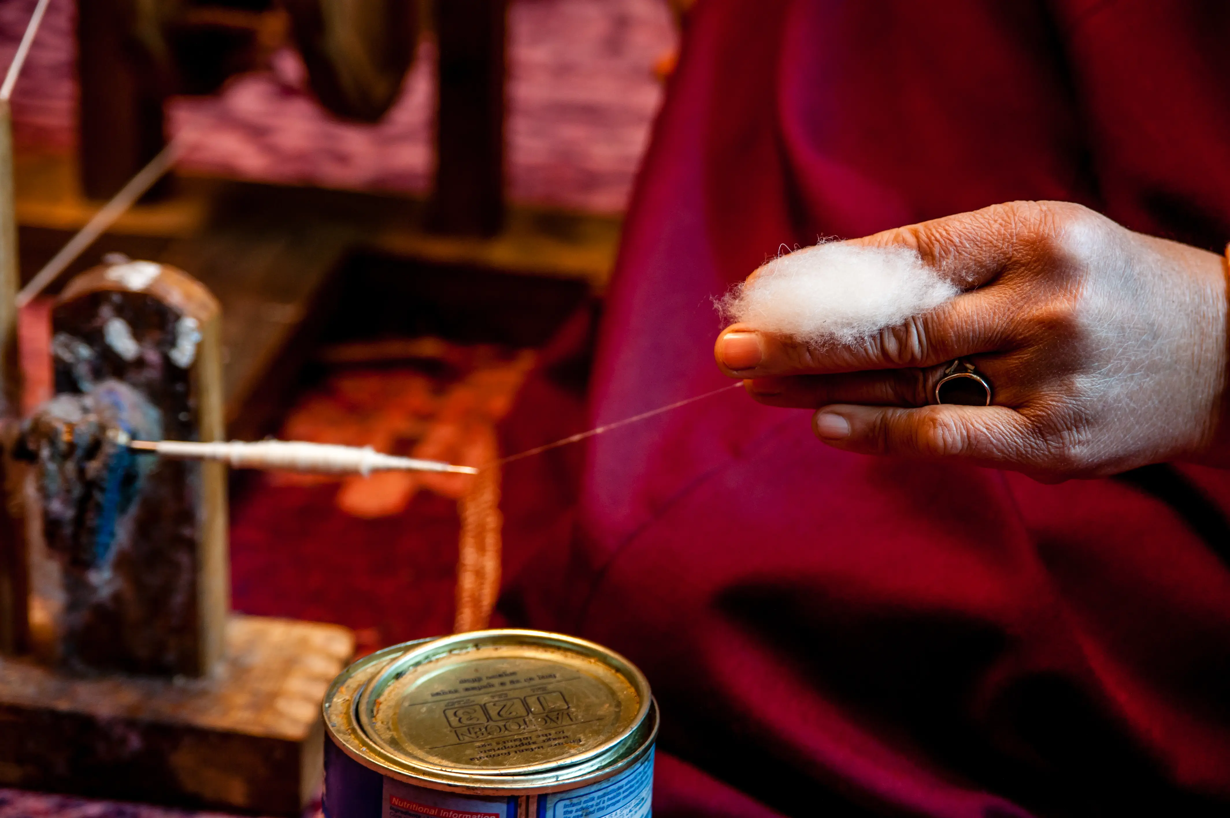 An artisan hand-spinning pashmina fibre onto a traditional spindle, seated on a red carpet