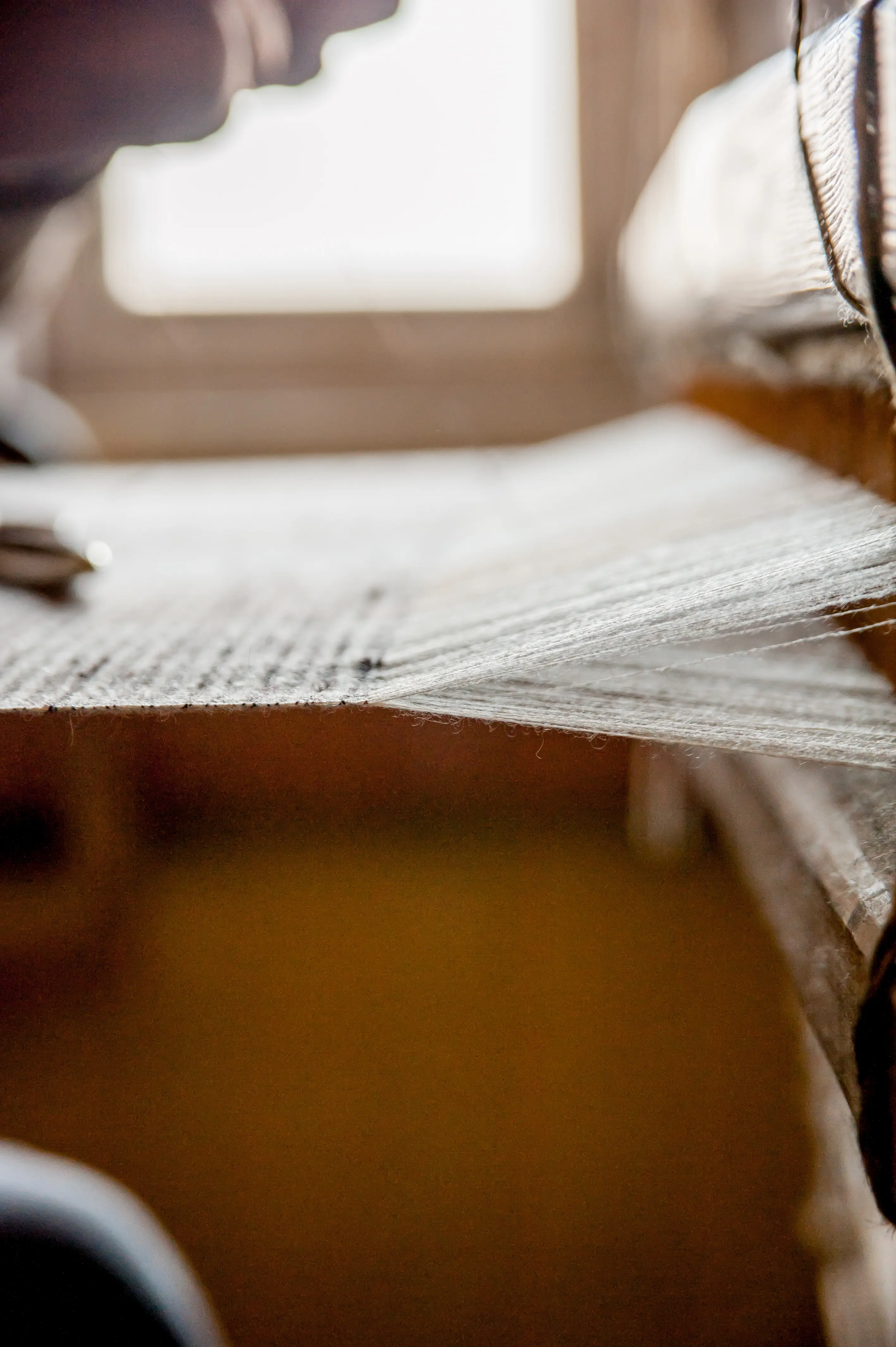 A macro detail of warp threads passing through a loom's reed